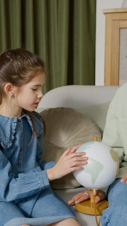 Een meisje bekijkt een wereldbol op de bank thuis