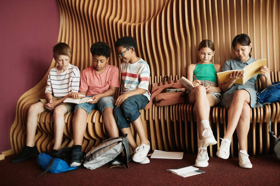 Diverse groep kinderen die samen een boek lezen op een bankje