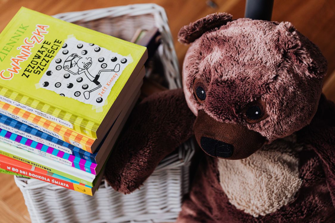 Stapel kleurrijke prentenboeken naast een knuffelbeer in een kinderkamer