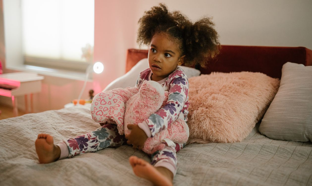 Een meisje in pyjama zit wakker op bed met haar knuffel
